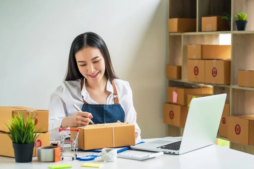 Asian small business owner holds a pen to write down addresses to deliver parcels to customer