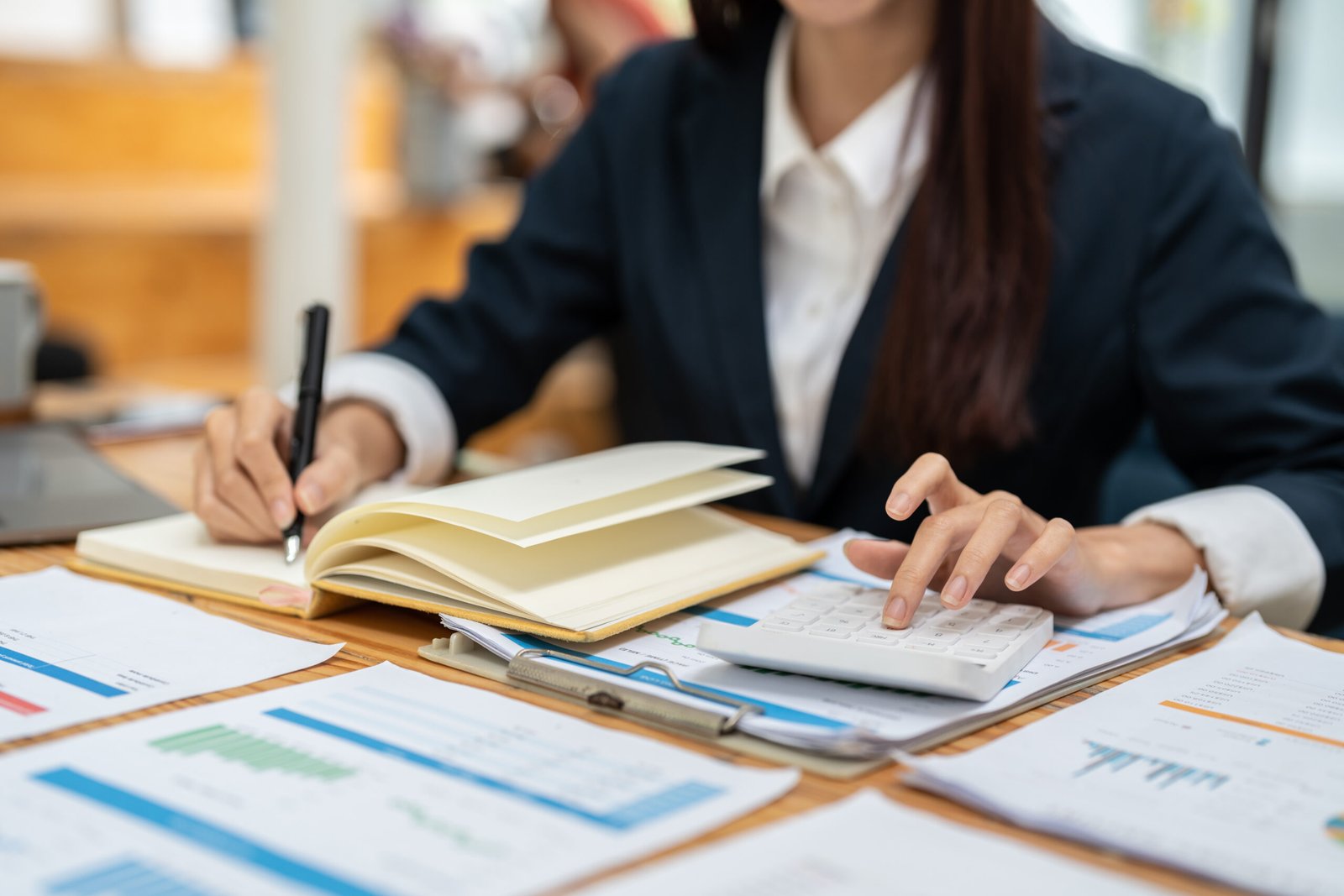 Woman making notes and using a calculator beside financial charts