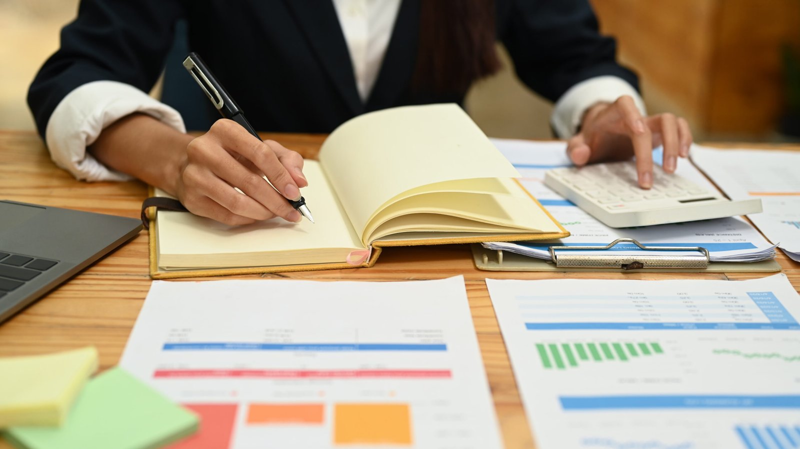 Business professional making notes beside a calculator and financial reports