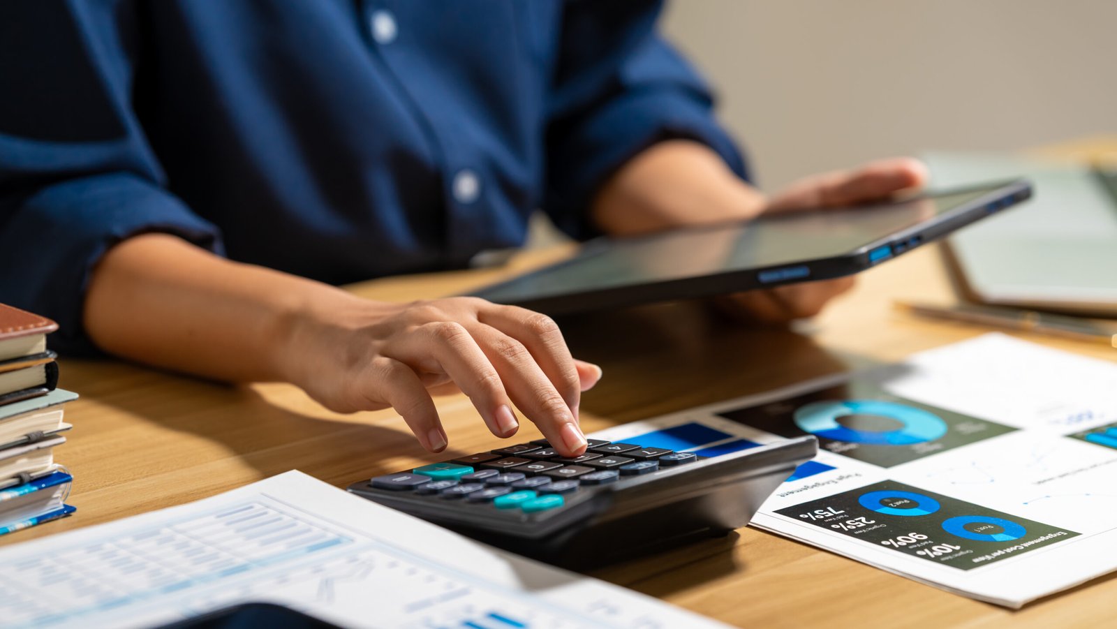 Professional using a calculator and tablet beside financial reports