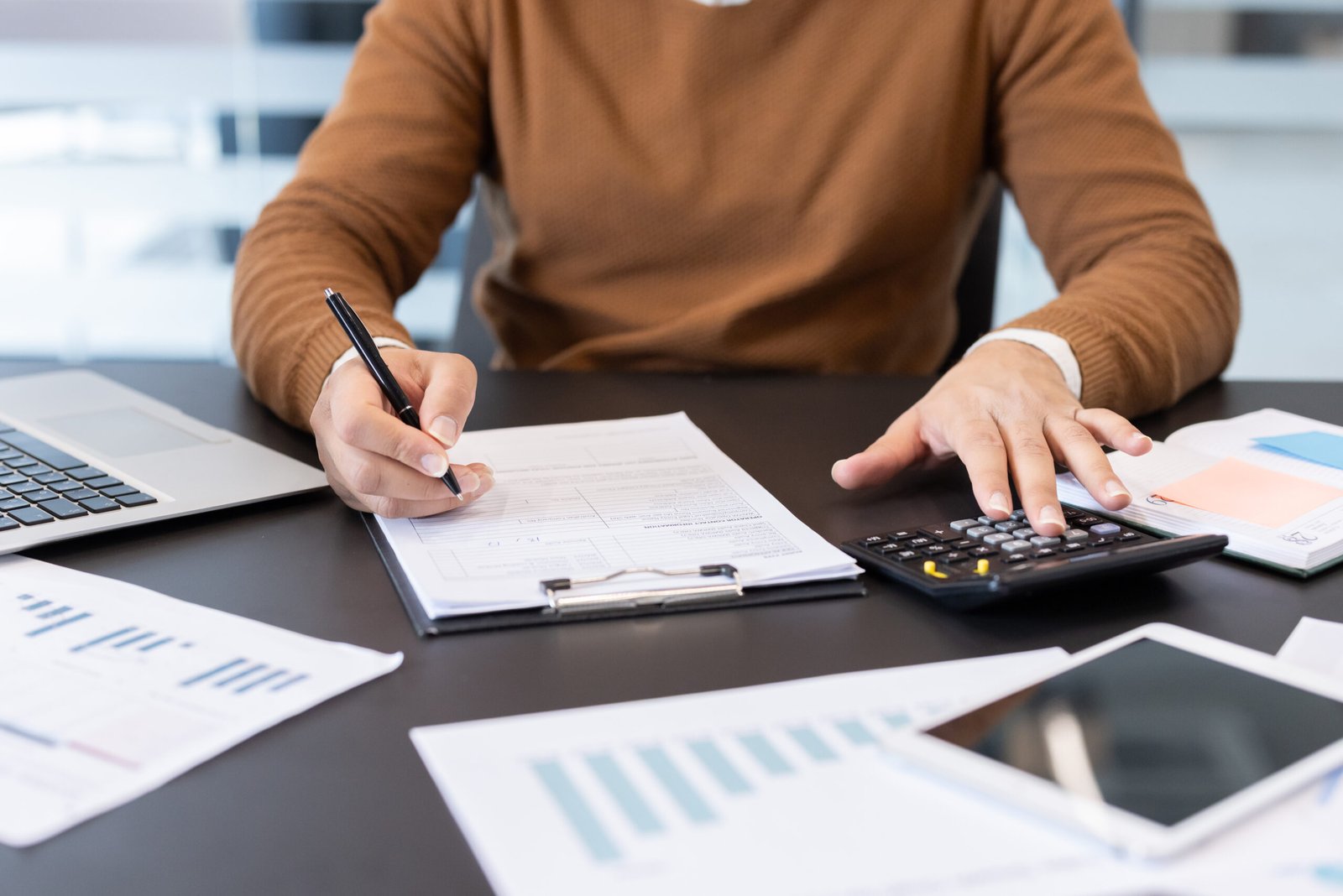 Professional reviewing financial documents with a calculator and laptop
